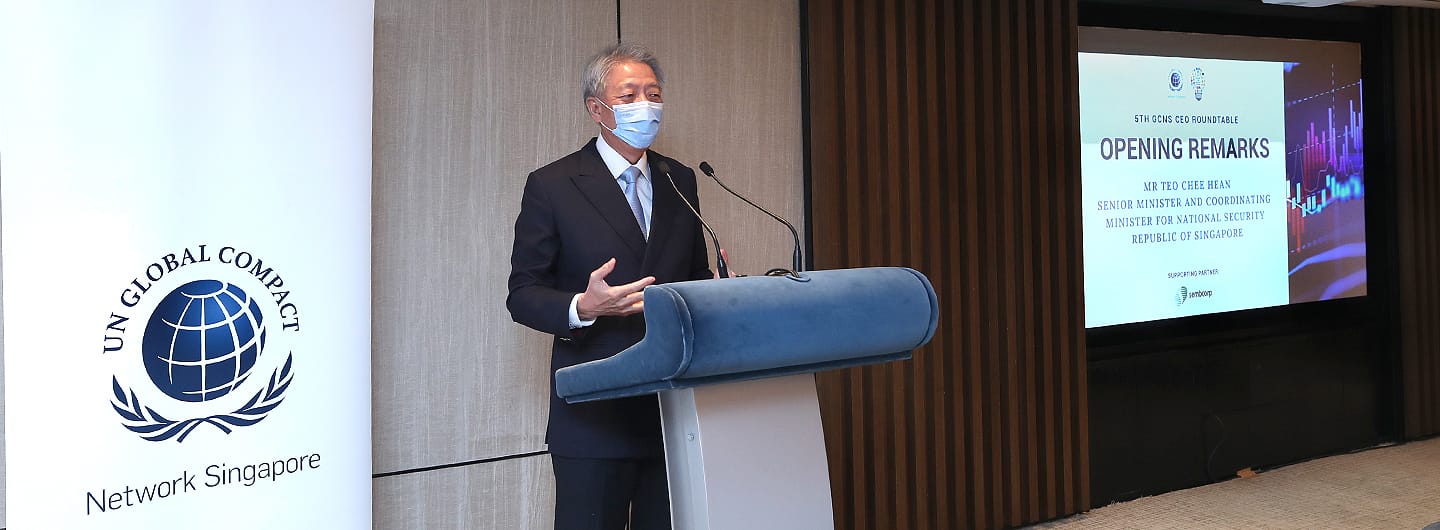 Man in suit and mask speaks at podium with UN Global Compact logo. Screen shows event and speaker info.